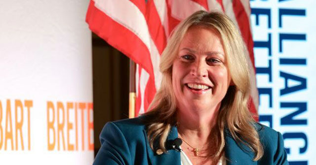 Janet Kelly speaking at a podium in front of an Alliance for a Better Future backdrop and American flag